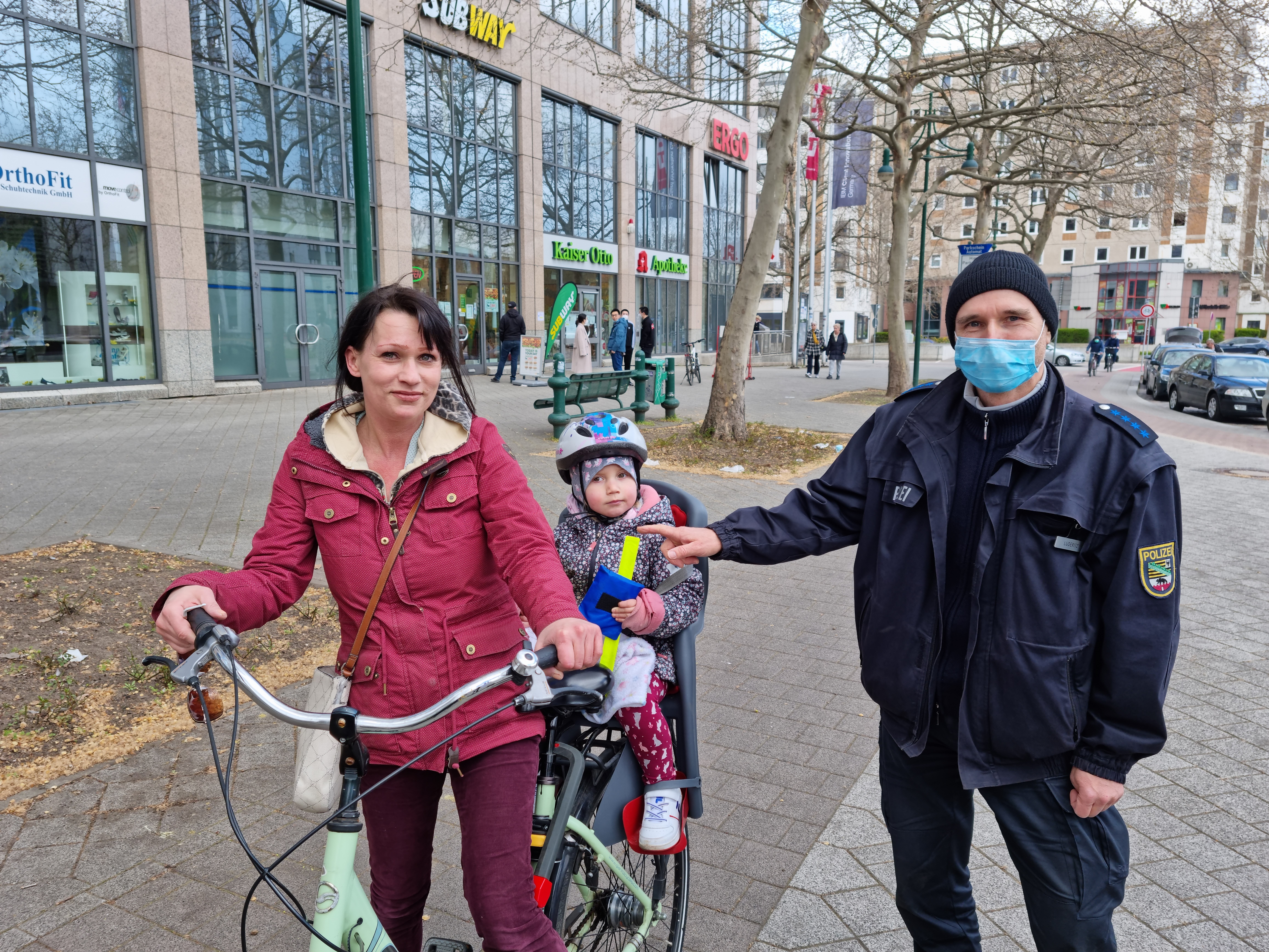 PHM Lüderitz übergibt einer Radfahrerin und deren Tochter Informationsmedien am Universitätsplatz in Magdeburg.